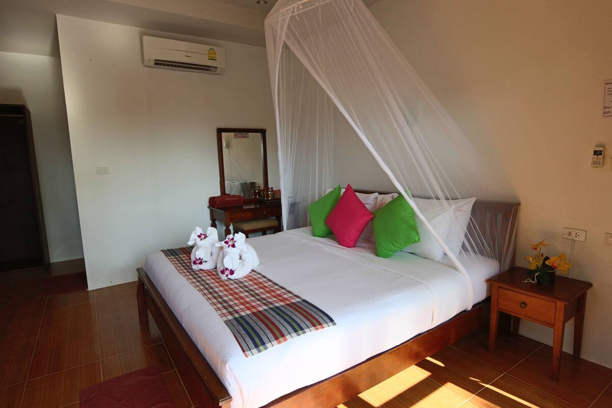 A neatly made bed with a canopy, pillows, a bedside table with a vase, and a mirror on the wall.