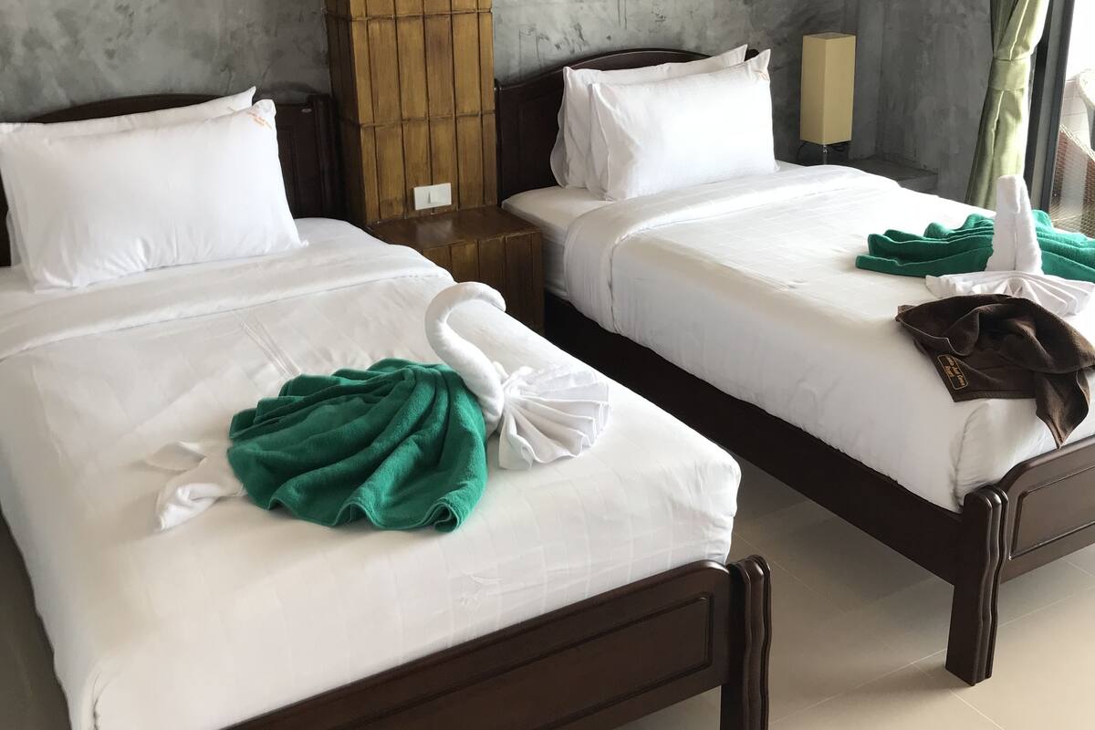 A hotel room with two beds, each with white linens and pillows, a wooden headboard, and a green towel on one bed.