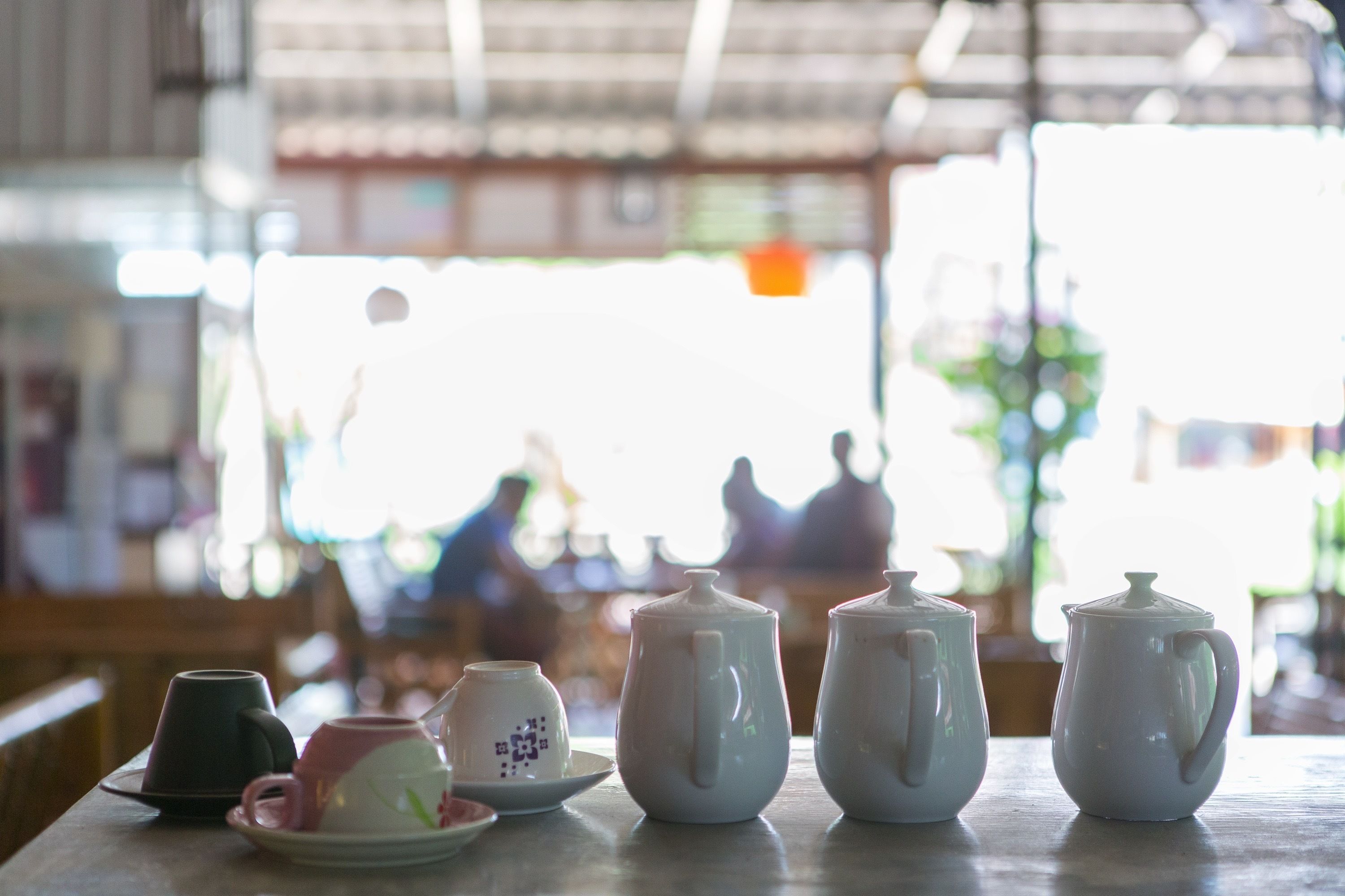 A table with various teapots and cups, likely in a cafe or restaurant setting.