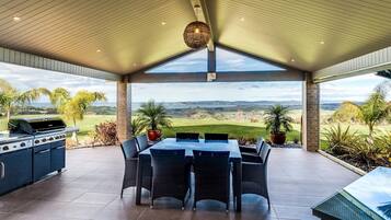 Enjoy al fresco dining with a panoramic view of the landscape from this outdoor dining area, featuring a large table, chairs, grill, and potted plants.
