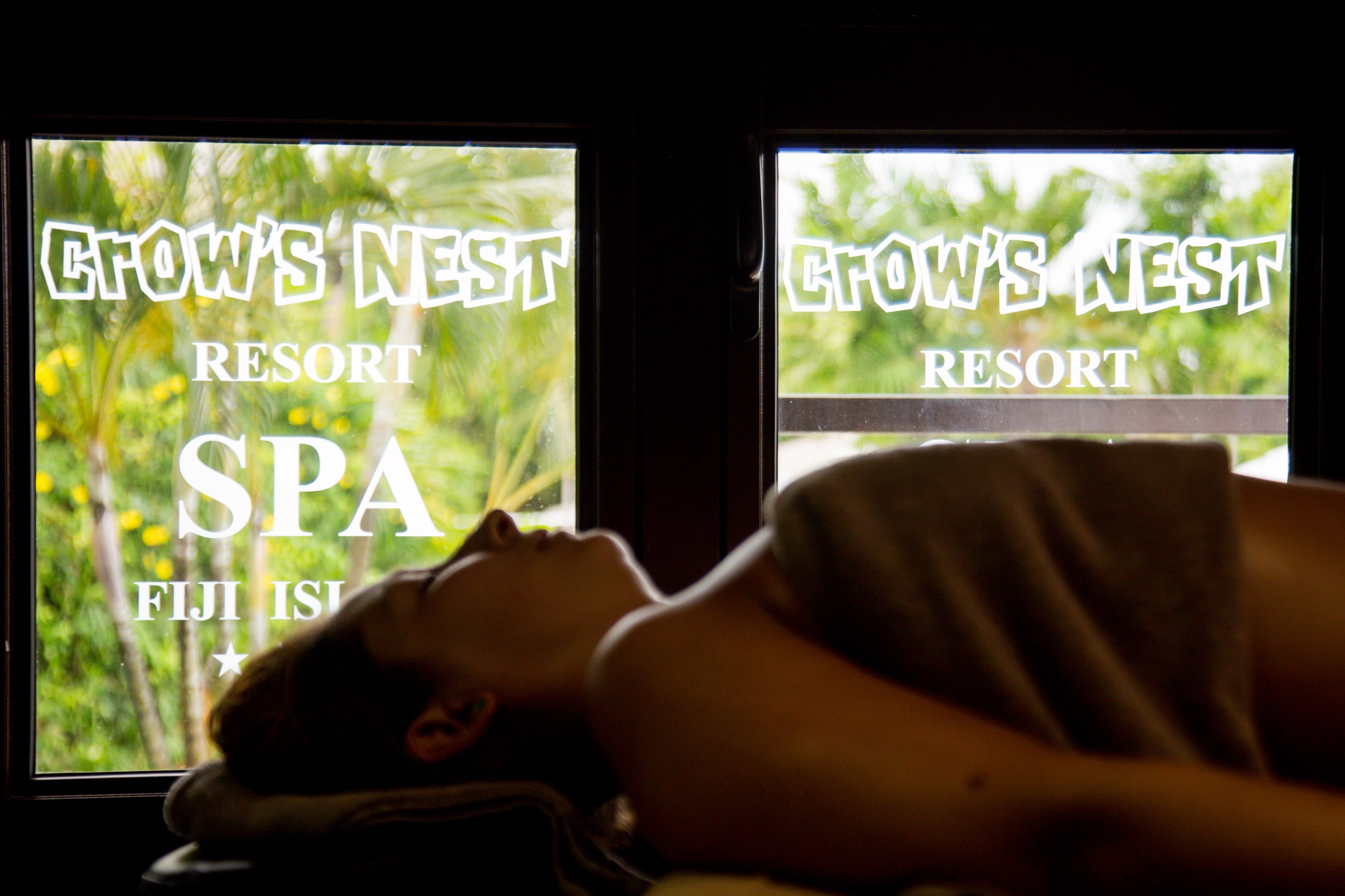 A person lying down with a window view of 'Grows Nest Resort' and 'Spa' signage.