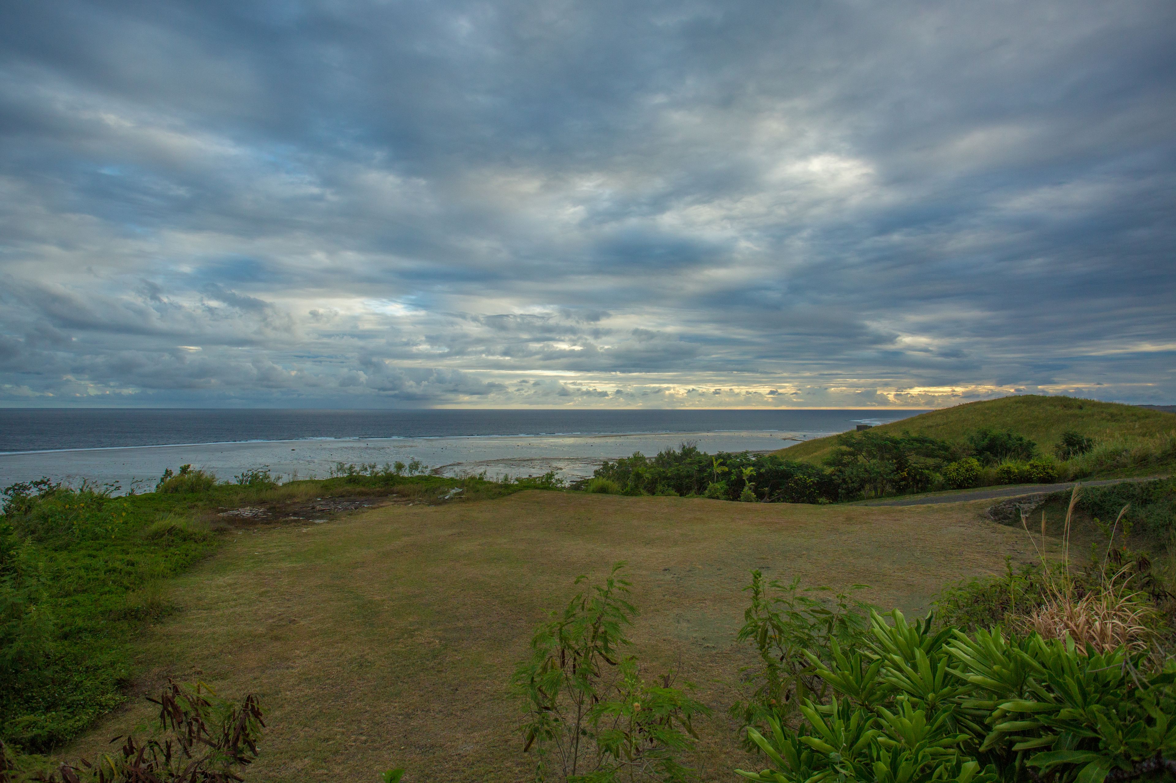 A grassy landscape with a view of the ocean and a cloudy sky.