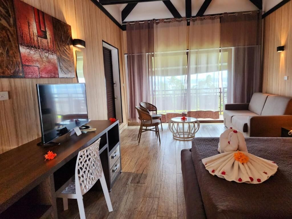 A room with a TV, a desk, a chair, a sofa, and a window with curtains.