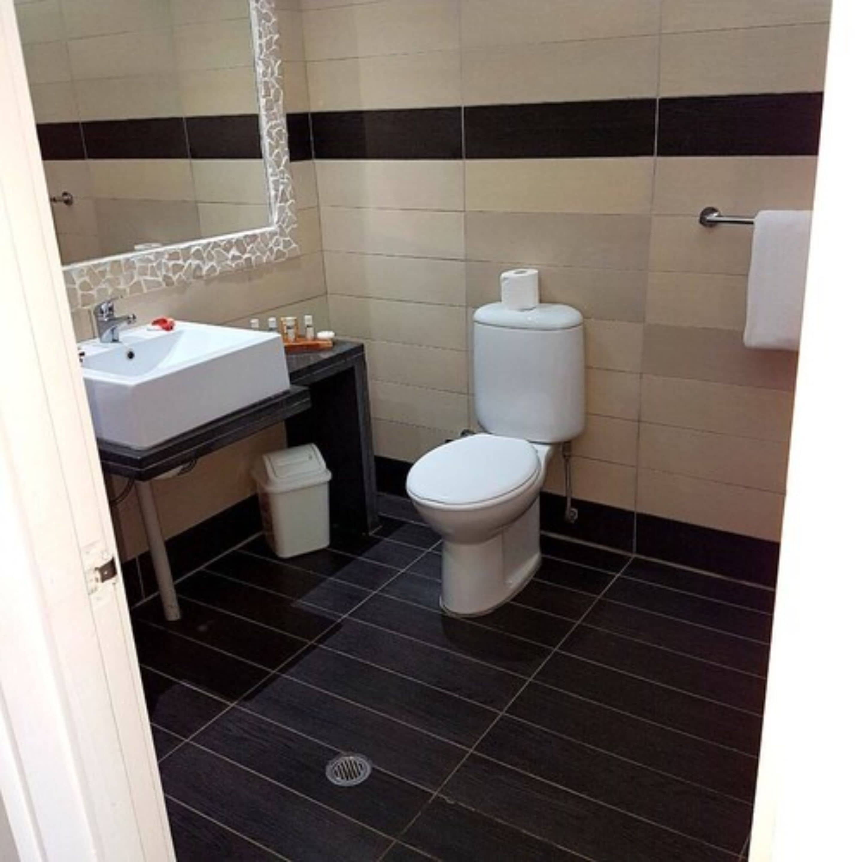 A modern bathroom with a white sink, black and white tiled walls, a toilet, and a trash bin.