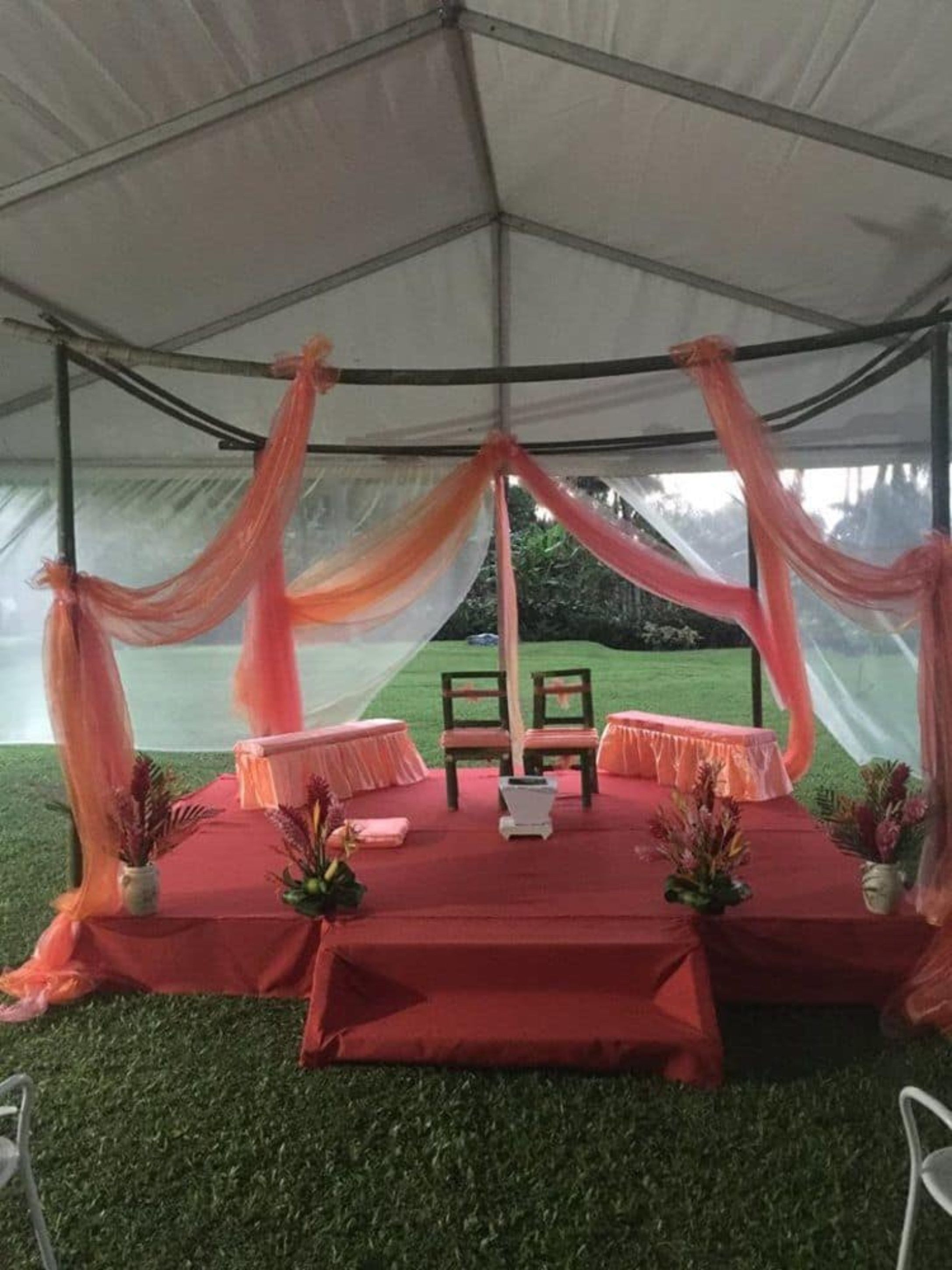 A tented outdoor event space with a stage, chairs, and floral arrangements.