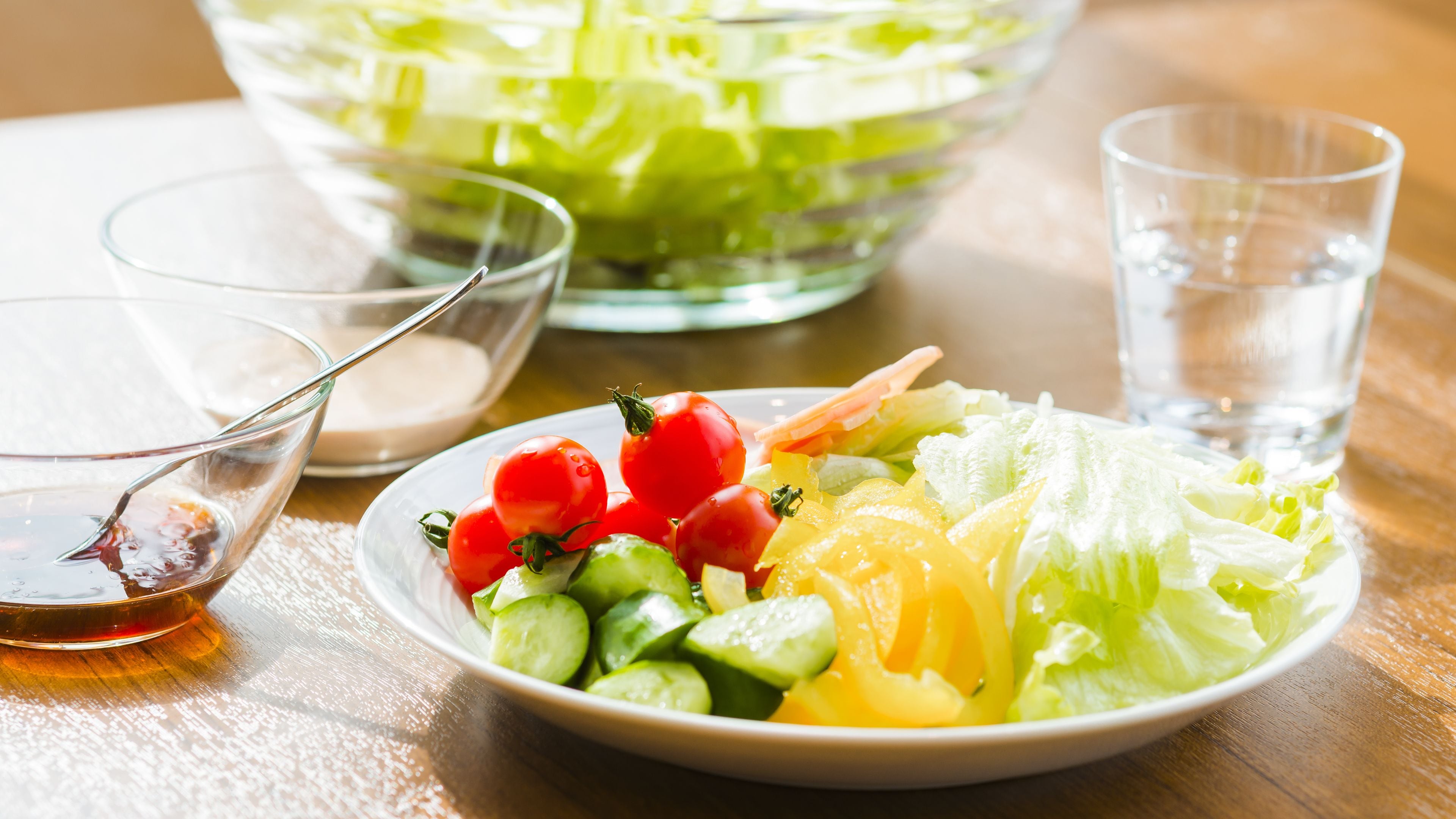 A salad bowl with various vegetables and a glass of water on a wooden table.