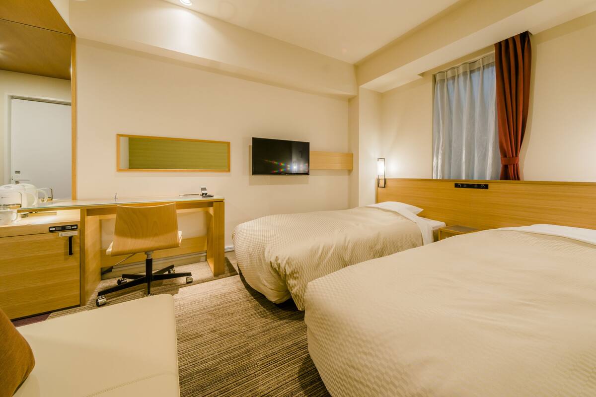 Ein Hotelzimmer mit zwei Betten, einem Schreibtisch, einem Stuhl, einer Kaffeemaschine und einem Fernseher.