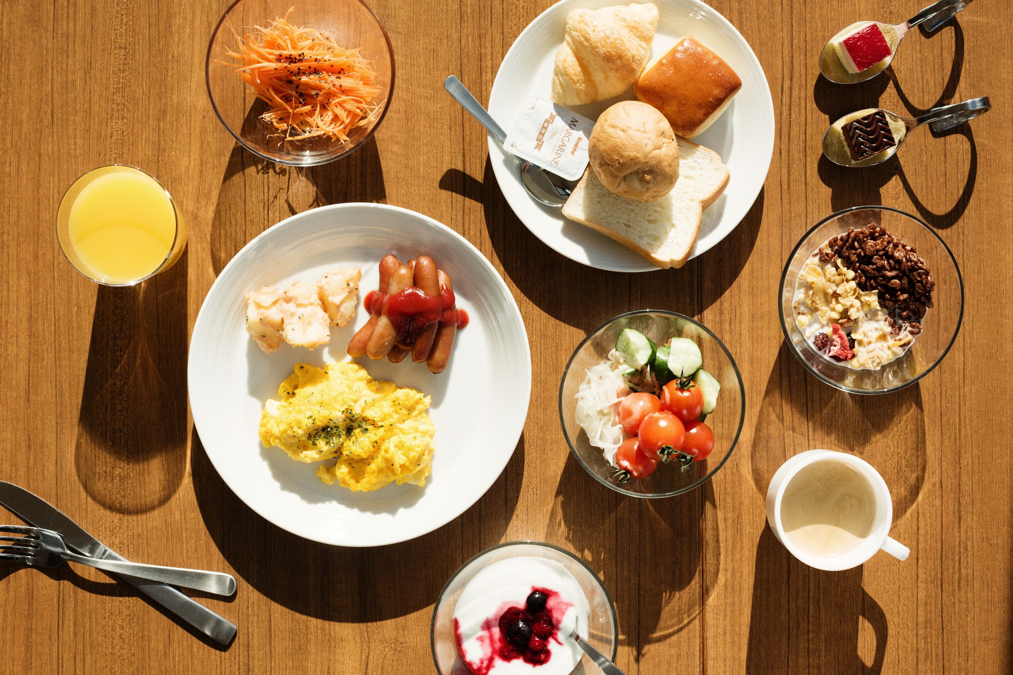 Una mesa de desayuno con huevos revueltos, tocino, tostadas y un tazón de ensalada de frutas.