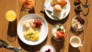 Una mesa de desayuno con huevos revueltos, tocino, tostadas y un tazón de ensalada de frutas.