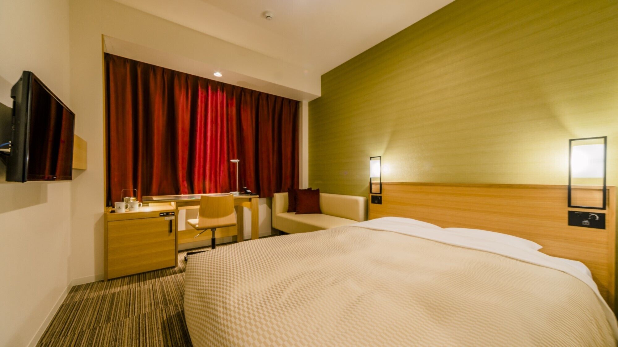 A hotel room with a bed, a desk, a chair, a TV, and a large window with red curtains.