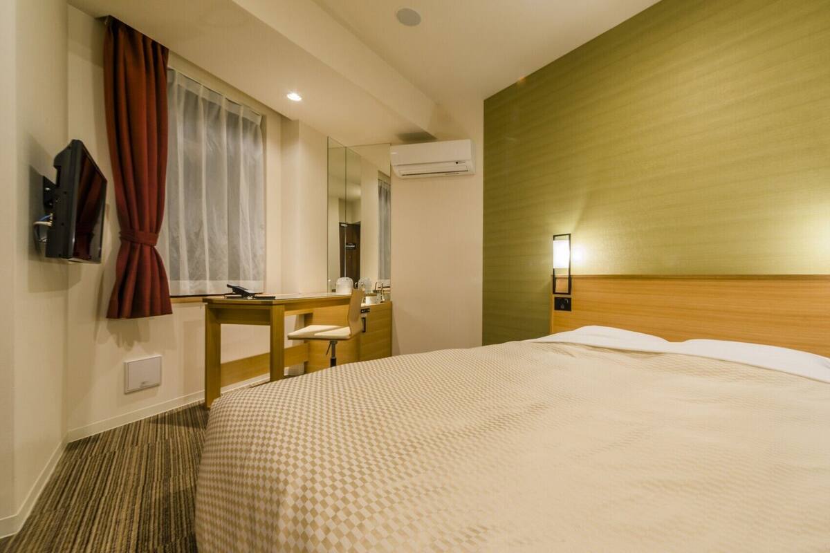 Ein Hotelzimmer mit einem großen Bett, einem Schreibtisch, einem Stuhl, einem Spiegel, einer Klimaanlage und zwei Wandleuchten.