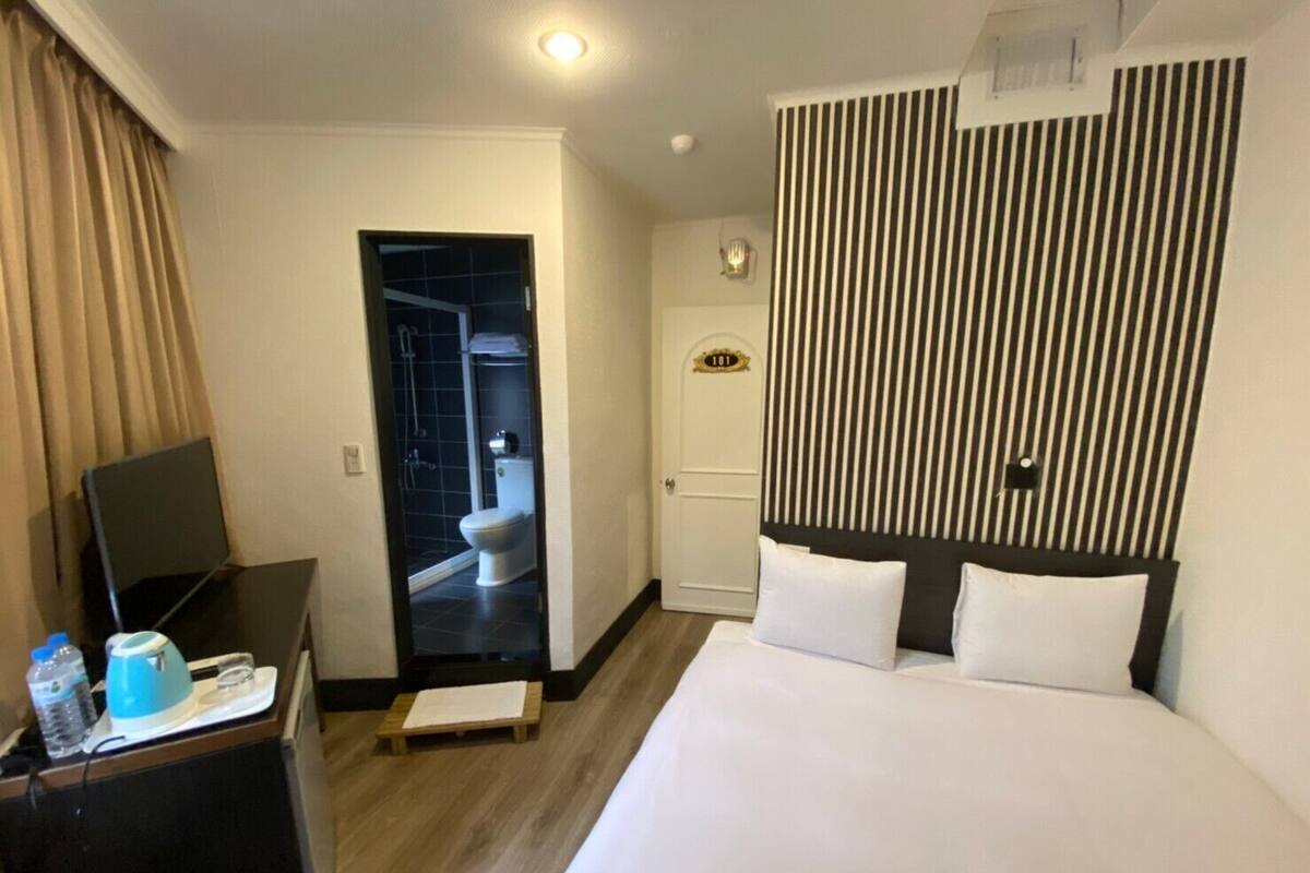 A hotel room with a bed, a desk with a chair, a television, and a bathroom visible through an open door.