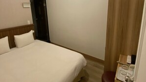 A hotel room with a large bed, a wooden headboard, a small desk with a chair, a mirror, and a toilet. - Hotel Queen (Taipei)