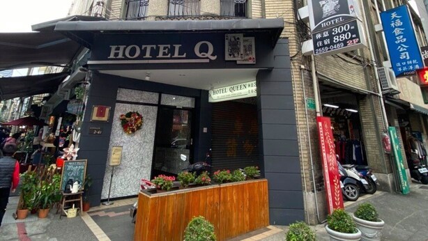 A building with a sign for HOTEL Q and HOTEL QUEEN. There are potted plants in front and a wooden bench. - Hotel Queen (Taipei)