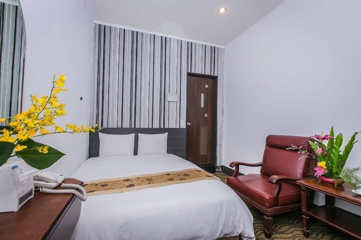 A hotel room with a bed, a chair, a desk with a phone, and a wall with vertical stripes.