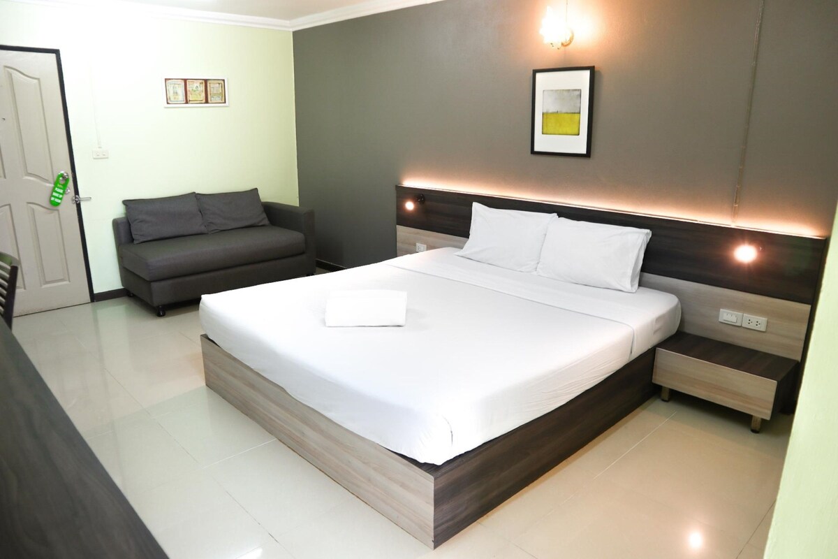 A modern hotel room with a large bed, a bedside table, a nightstand, a sofa, and a door.