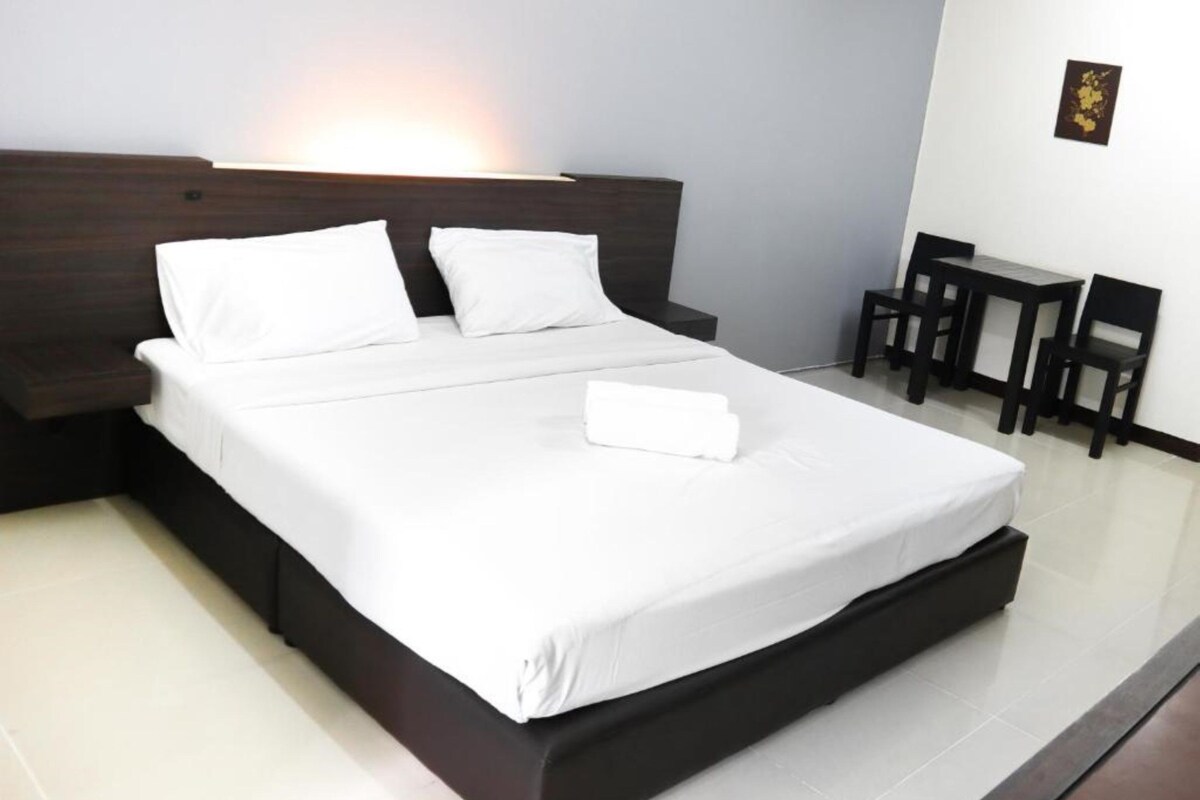 A modern hotel room with a large bed, a bedside table, and a small desk with chairs.