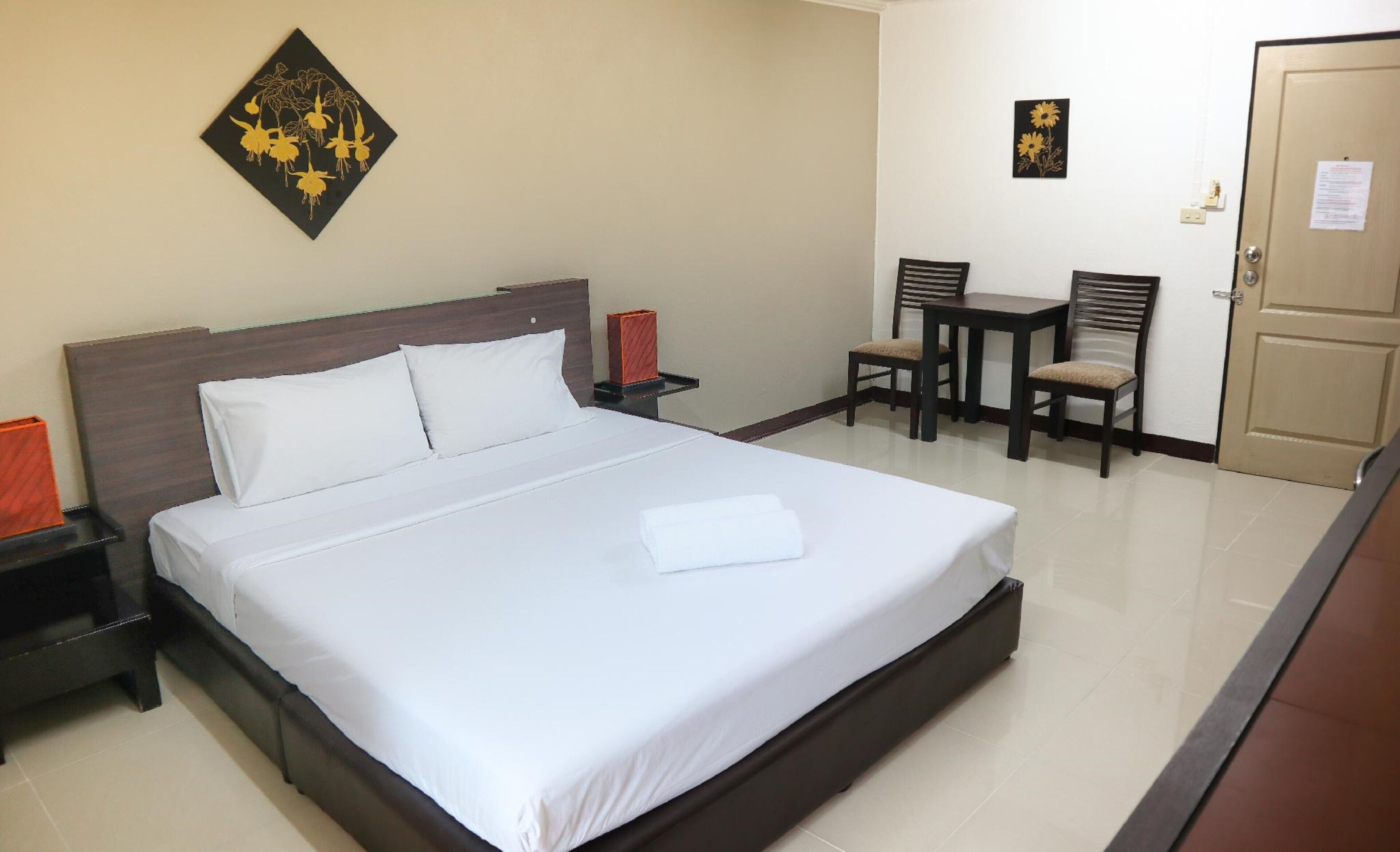 Una habitación de hotel con una cama grande, una mesita de noche, una silla, una pequeña mesa y una puerta.