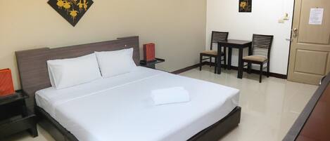 Una habitación de hotel con una cama grande, una mesita de noche, una silla, una pequeña mesa y una puerta.