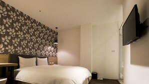 Ett hotellrum med en säng, en tv som är monterad på väggen och en tapet med mönster på väggen bakom sängen.