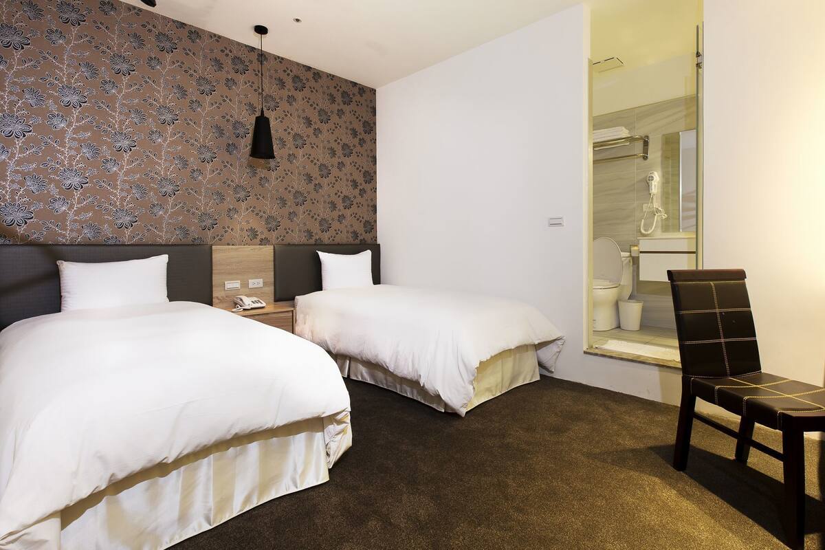A hotel room with two beds, a shower, and a chair.