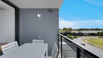 Een balkon met een witte tafel en stoelen, een grijze muur en uitzicht op een woongebied.
