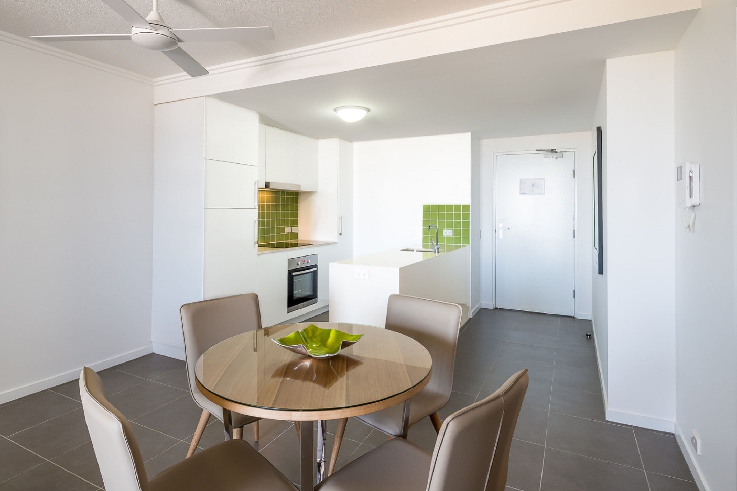 A modern kitchen with white cabinets, a green backsplash, and a built-in oven.