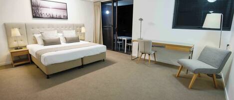 A hotel room with a large bed, a desk, a chair, a ceiling fan, and a window with a view.