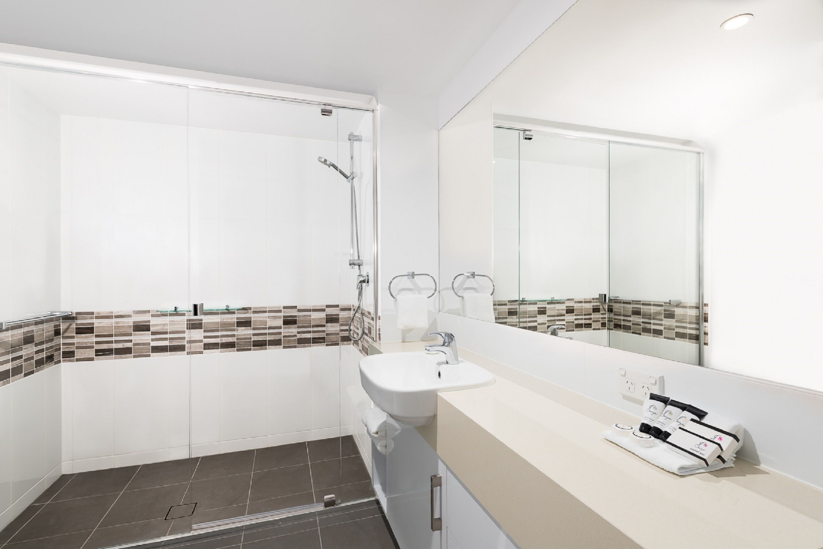 Een moderne badkamer met een douche, een wastafel en een grote spiegel.