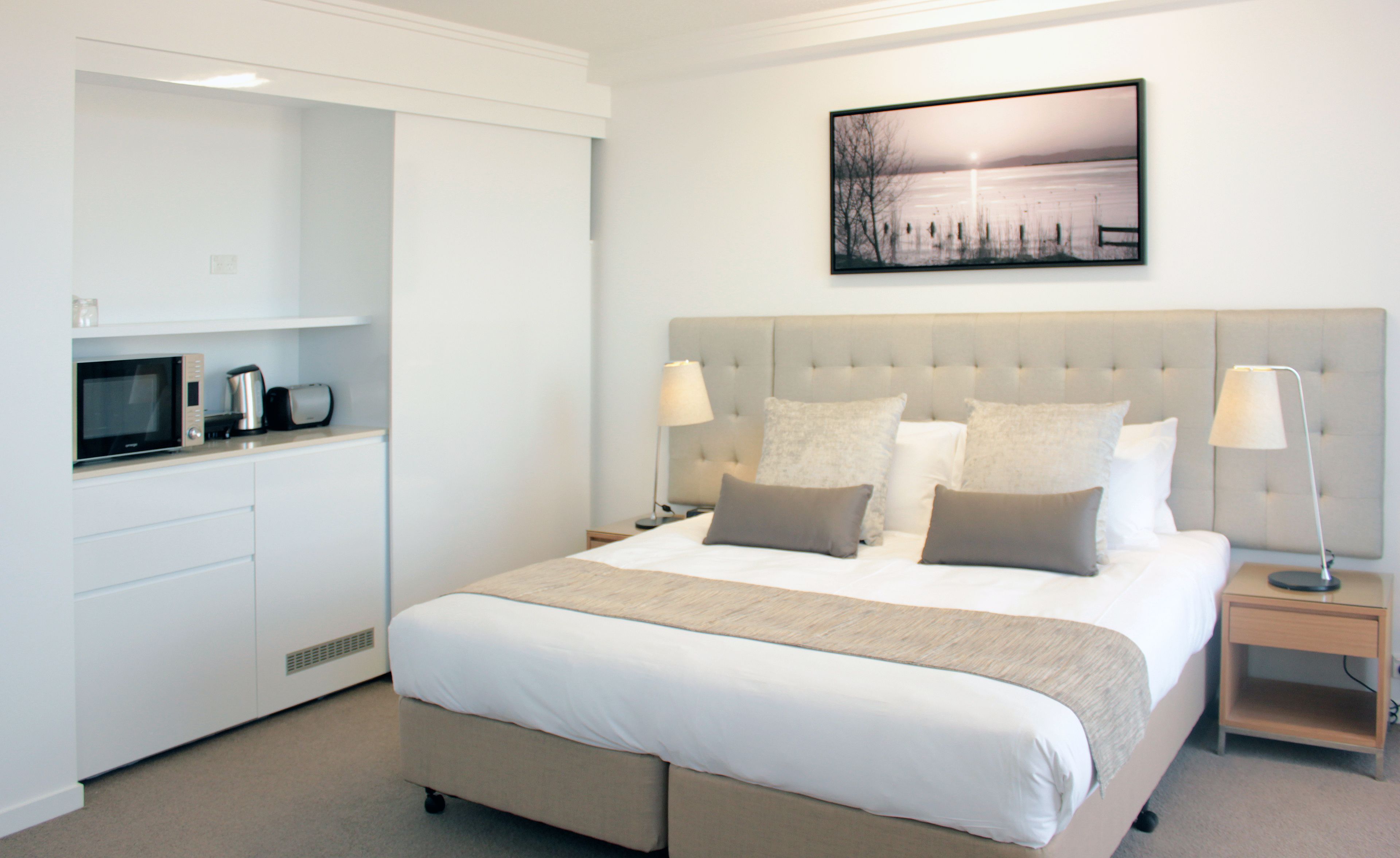 A modern hotel room with a large bed, a flat-screen TV, a microwave, and a coffee maker on the counter.