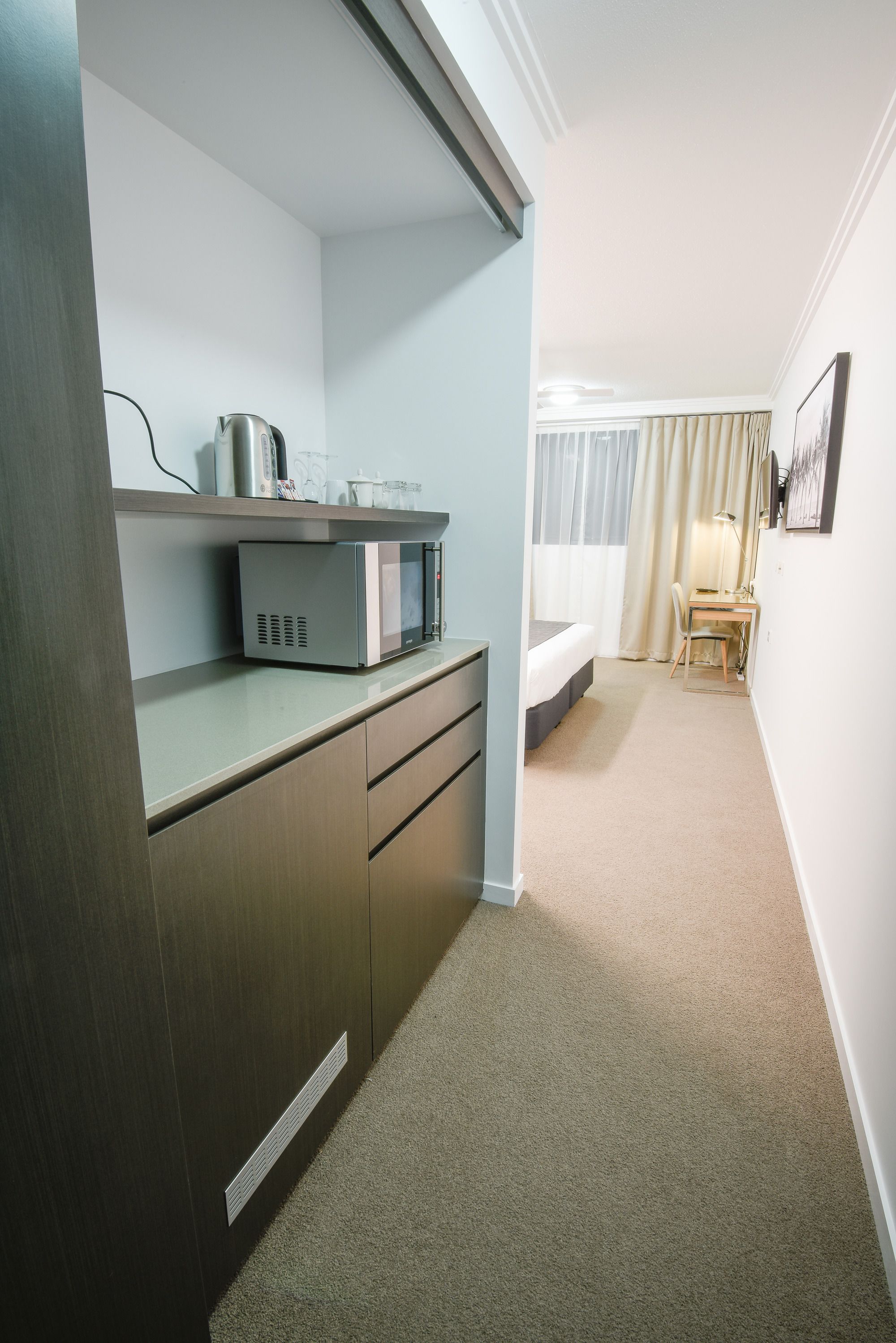 Una habitación de hotel compacta con kitchenette, una cama, un escritorio y una silla.