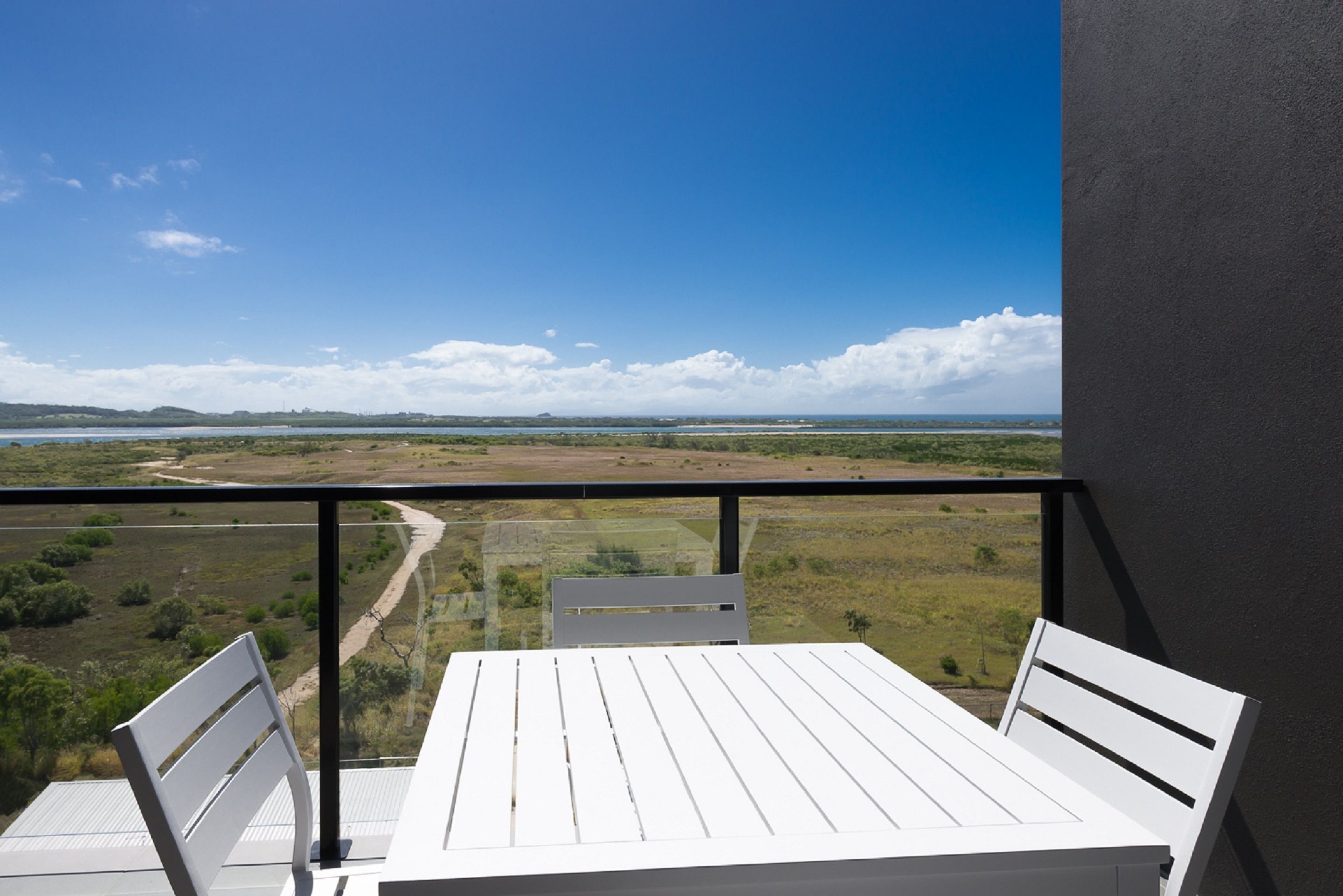 Un balcón con mesa y sillas, que ofrece vistas a un paisaje con una masa de agua y colinas distantes.