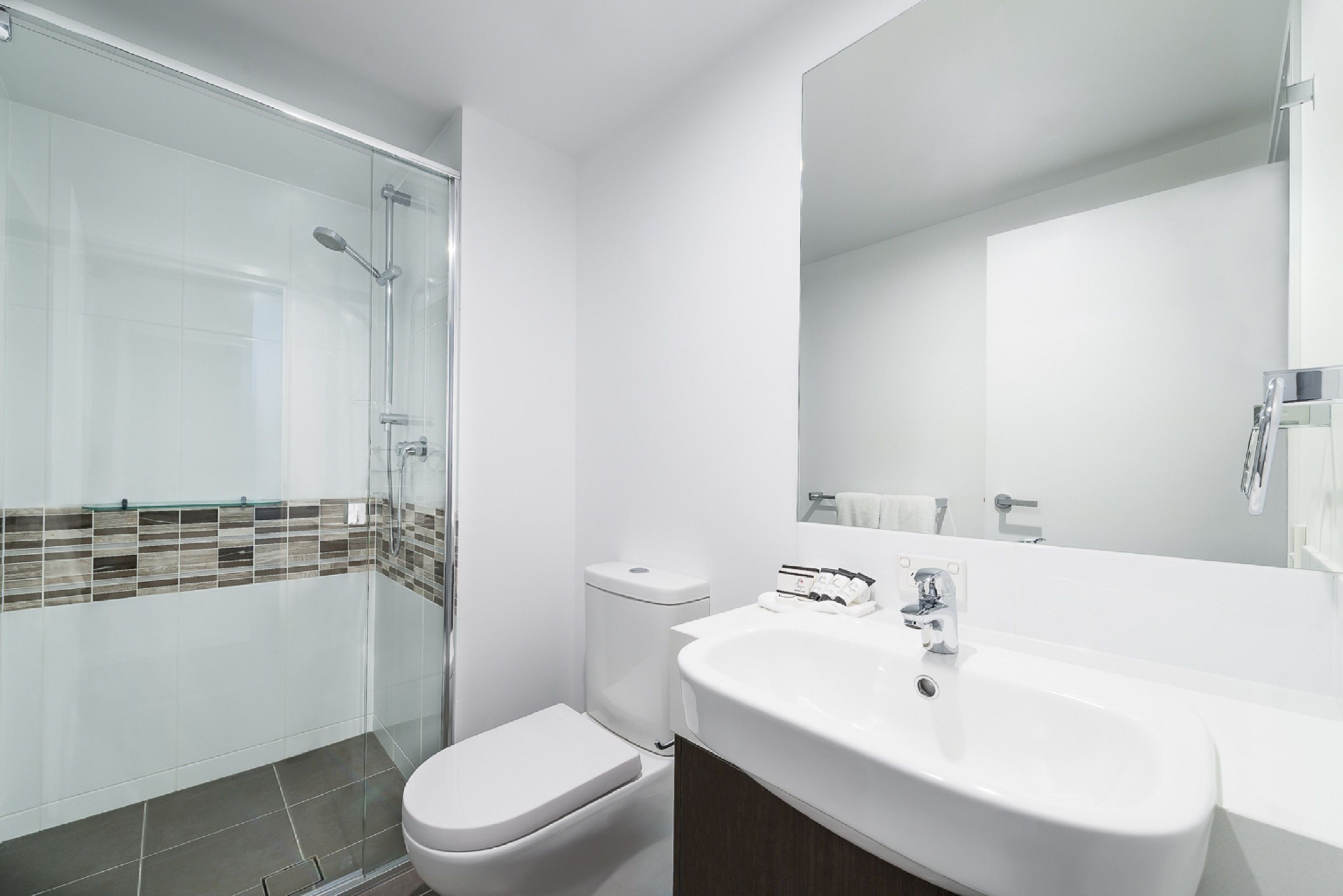 A modern bathroom with a glass shower enclosure, a white toilet, and a large sink with a mirror.