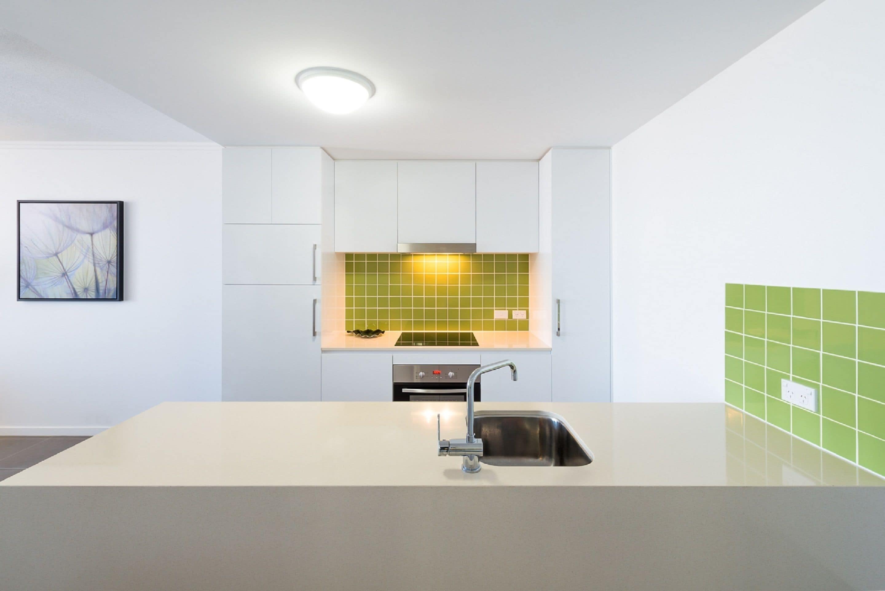 A modern kitchen with white cabinets, a green backsplash, and a stainless steel sink.