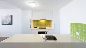 A modern kitchen with white cabinets, a green backsplash, and a stainless steel sink.