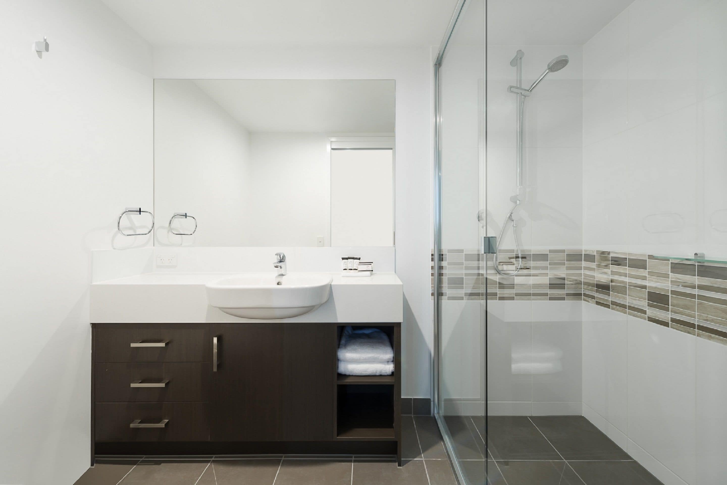 Une salle de bain moderne avec un lavabo blanc, un meuble sombre et une douche à parois de verre.