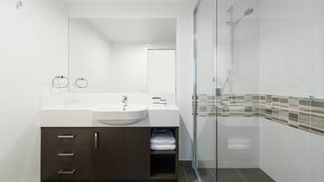 Une salle de bain moderne avec un lavabo blanc, un meuble sombre et une douche à parois de verre.