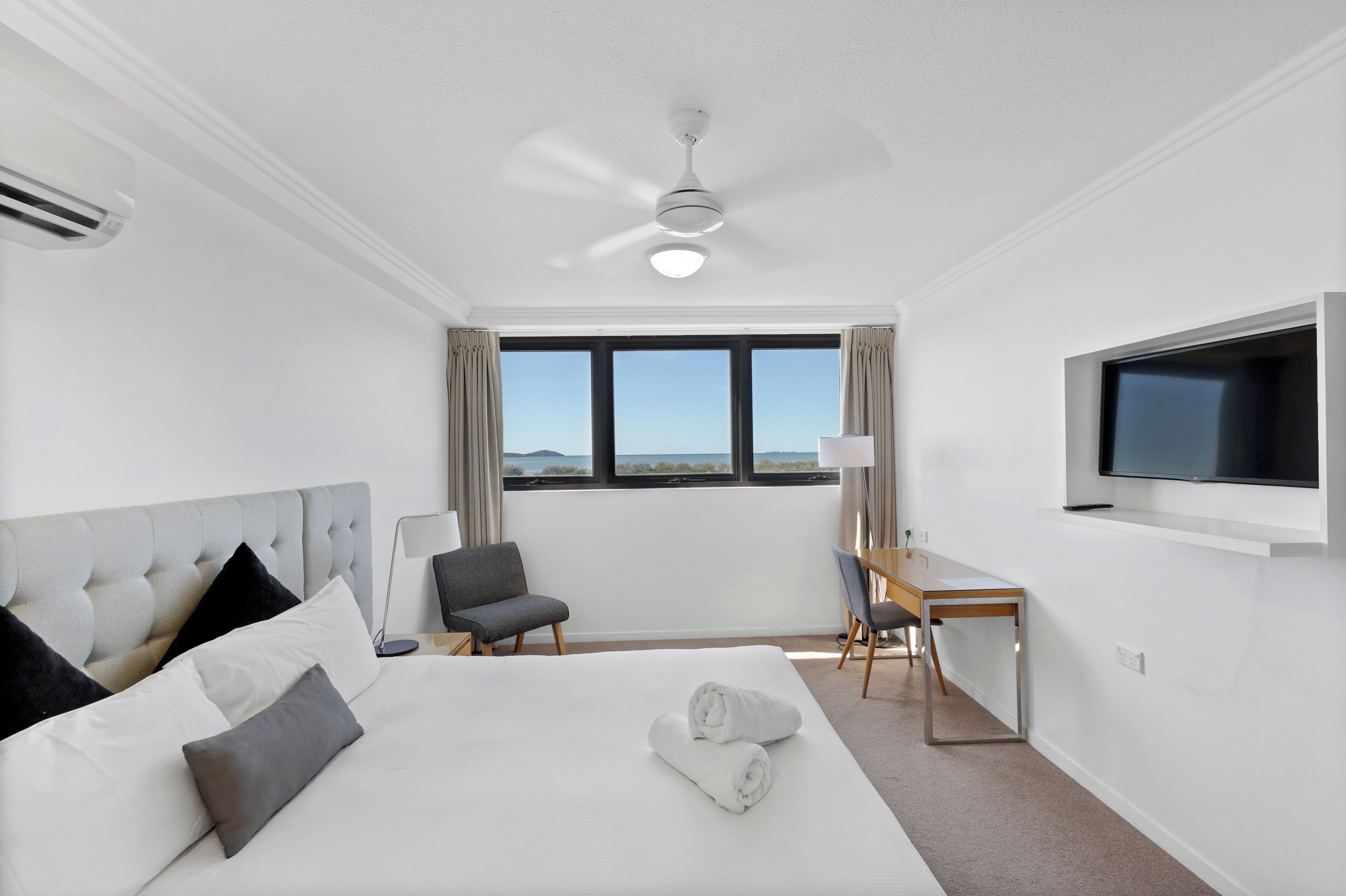 Habitación de hotel con una cama grande, un escritorio, una silla, un televisor y vistas al exterior.