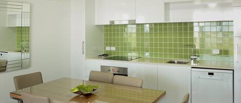 Una cocina moderna con armarios blancos, salpicadero verde y un comedor con mesa y sillas.