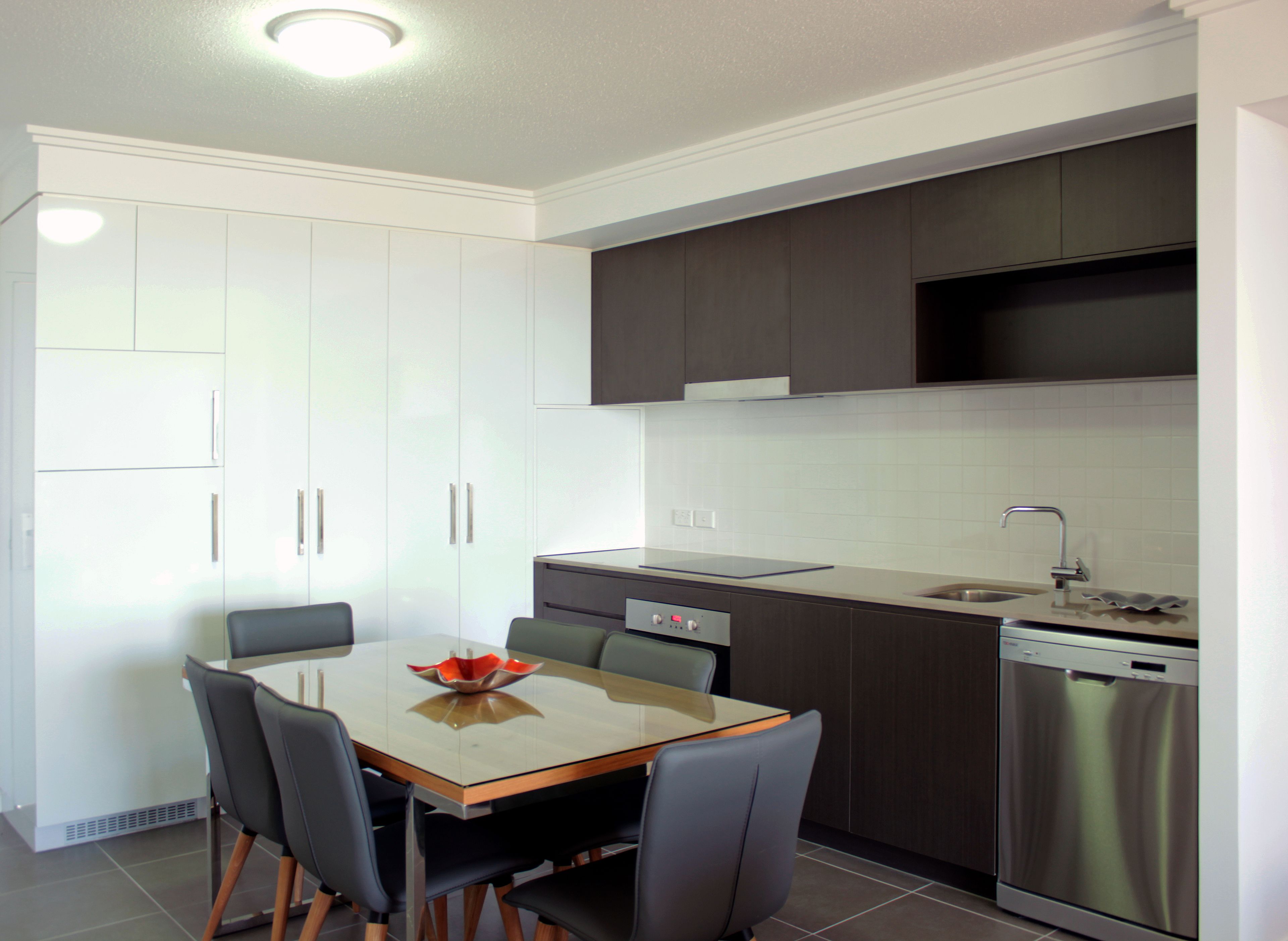 A modern kitchen with white cabinets, a stainless steel dishwasher, and a dining area with a table and chairs.