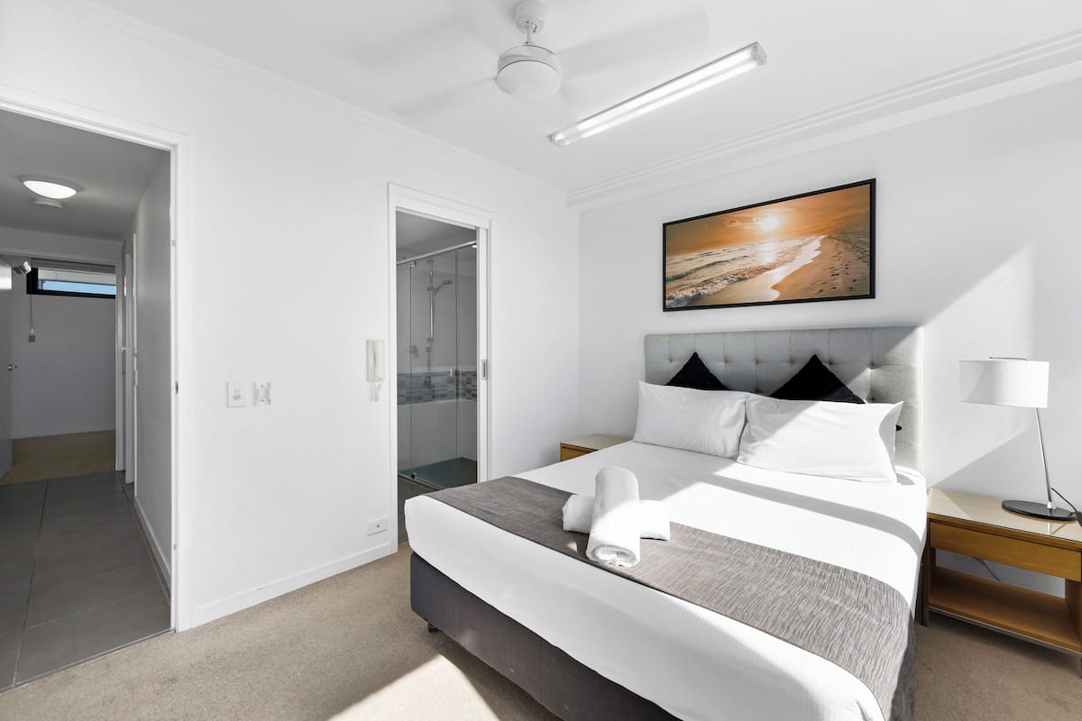 A hotel room with a bed, a nightstand, a lamp, and a painting on the wall.