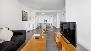 En moderne stue med sofa, sofabord og TV. I baggrunden ses et spiseområde med stole og bord.