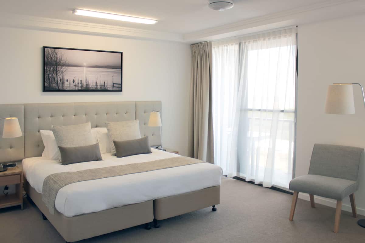 A neatly arranged hotel room with a large bed, bedside lamps, a chair, and a window with curtains.