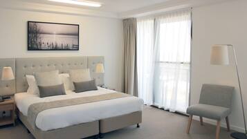A neatly arranged hotel room with a large bed, bedside lamps, a chair, and a window with curtains.