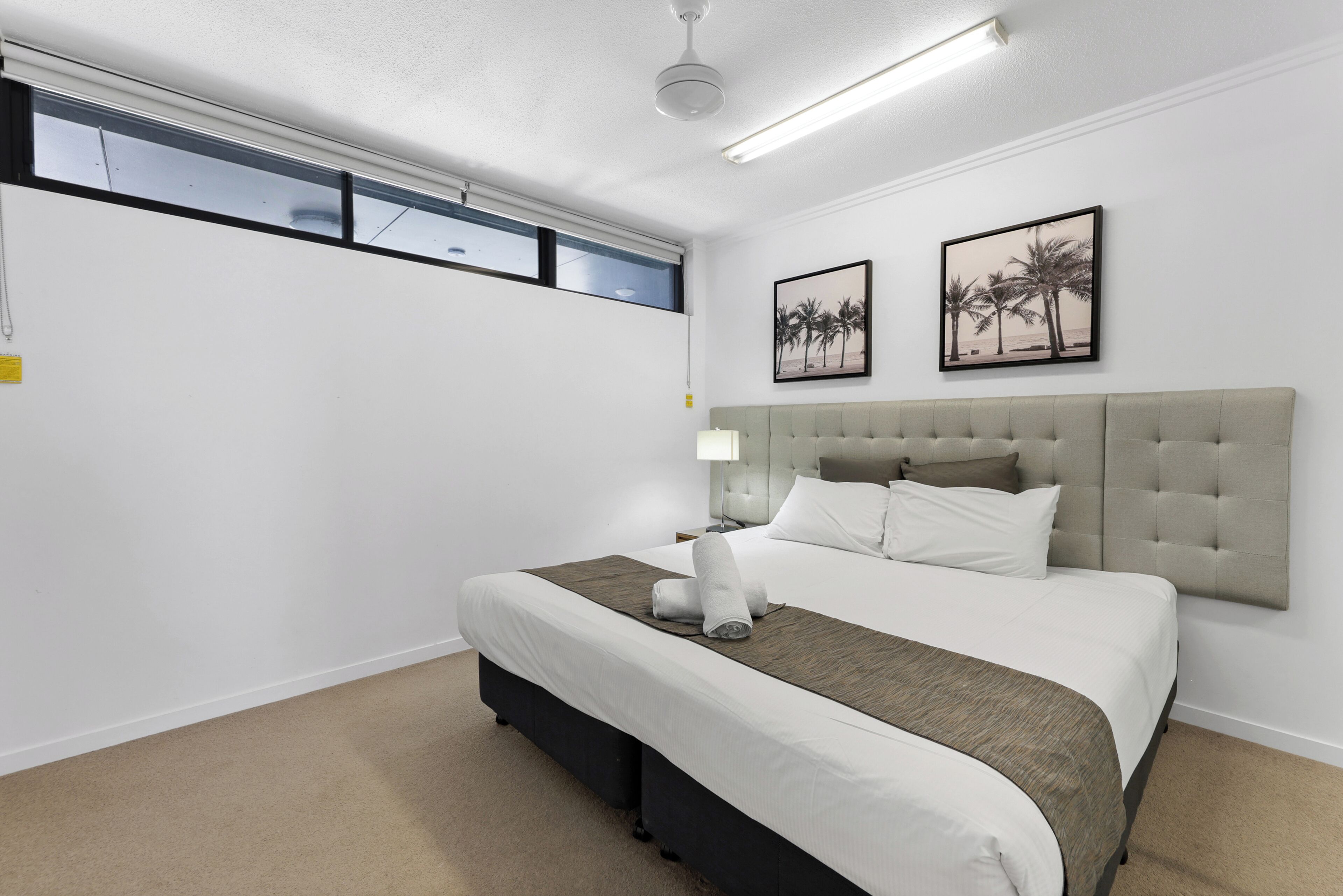 Une chambre à coucher bien aménagée, avec un grand lit, une tête de lit, deux tableaux accrochés au mur et une fenêtre avec des stores.