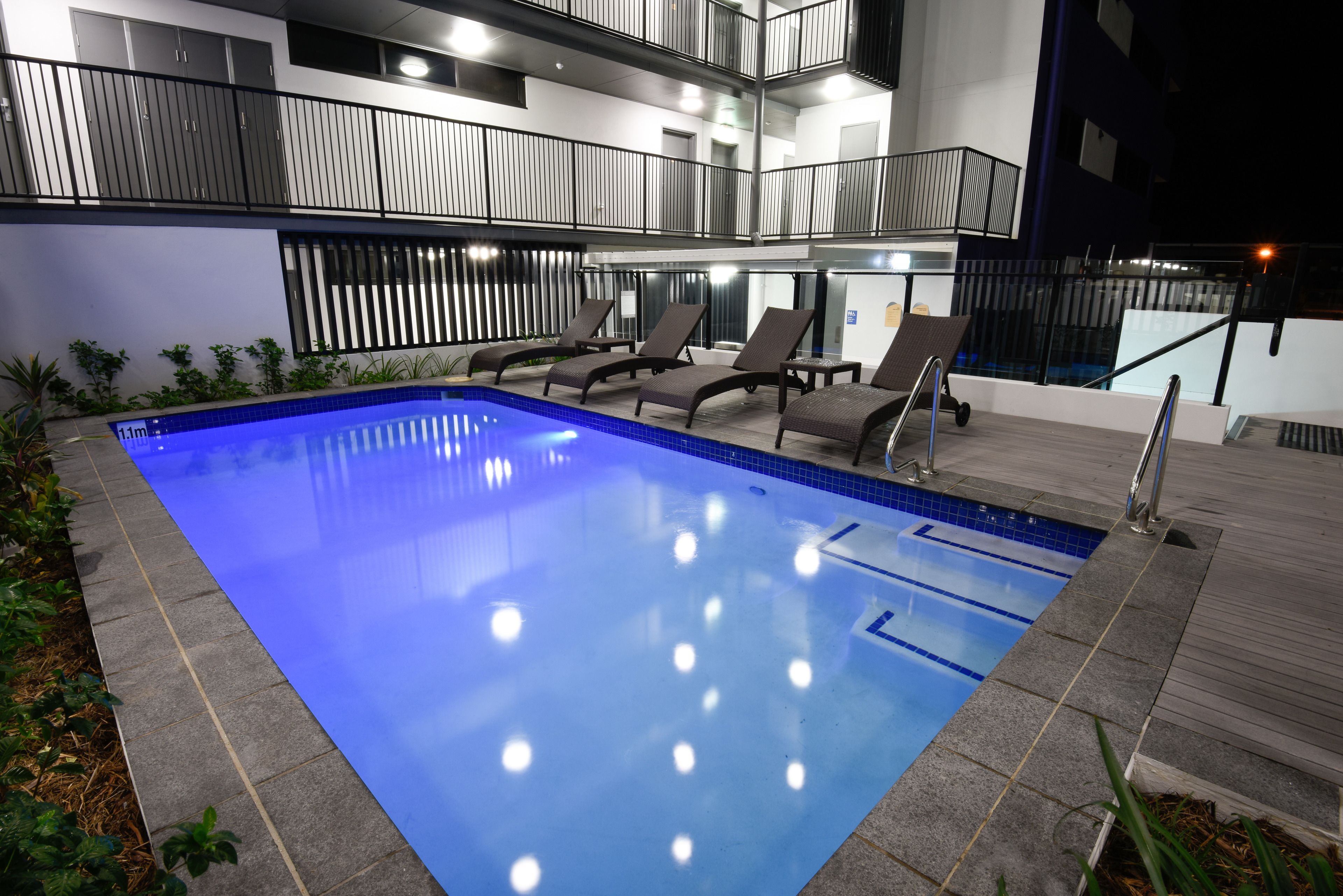 Una piscina con sillones de descanso y un balcón de varios niveles.