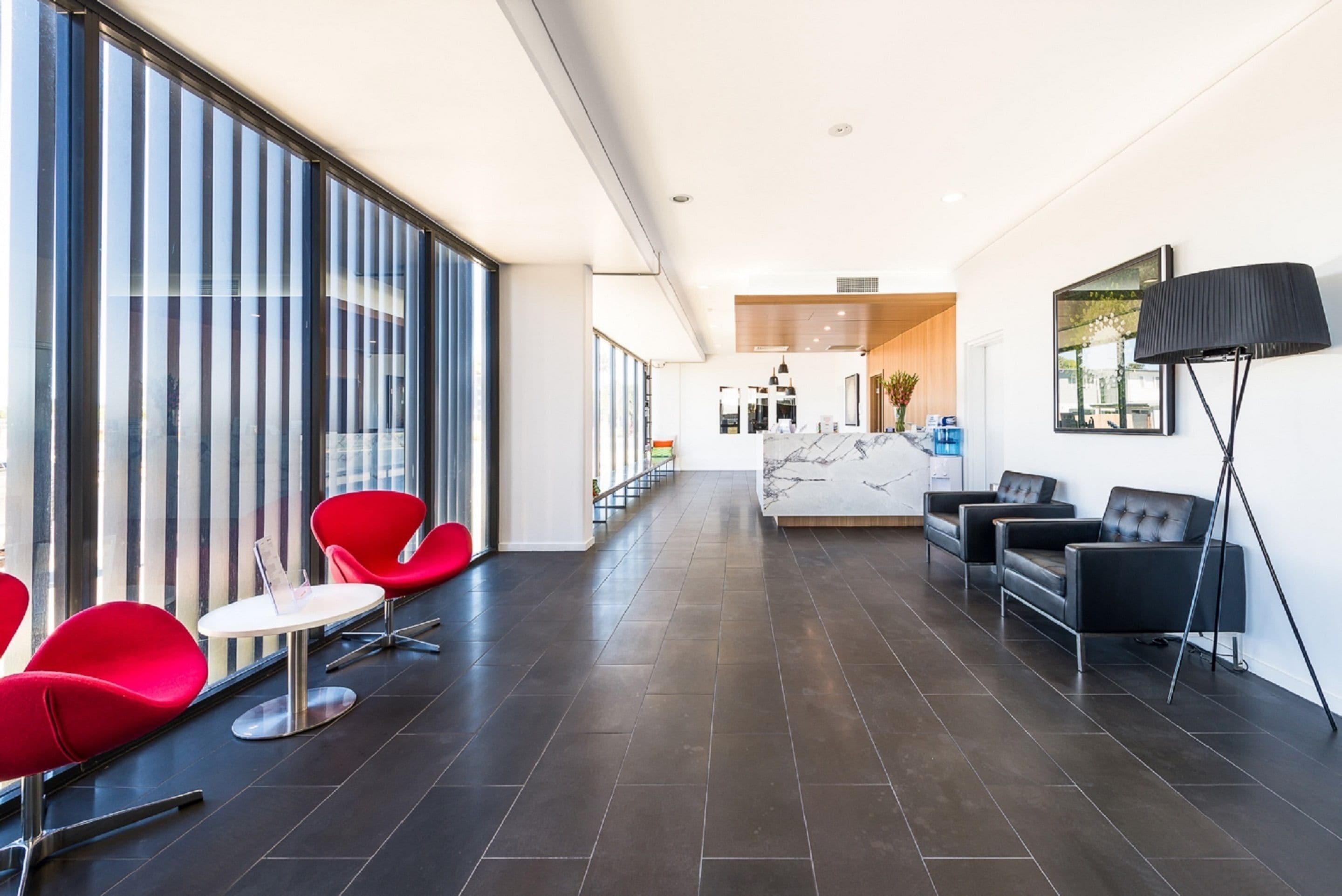 A modern hotel lobby with a long corridor, red and black seating areas, and a marble reception desk.