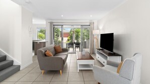 Una sala moderna con un sofá gris, una mesa de centro, un televisor de pantalla plana y una escalera que lleva a un espacio al aire libre.