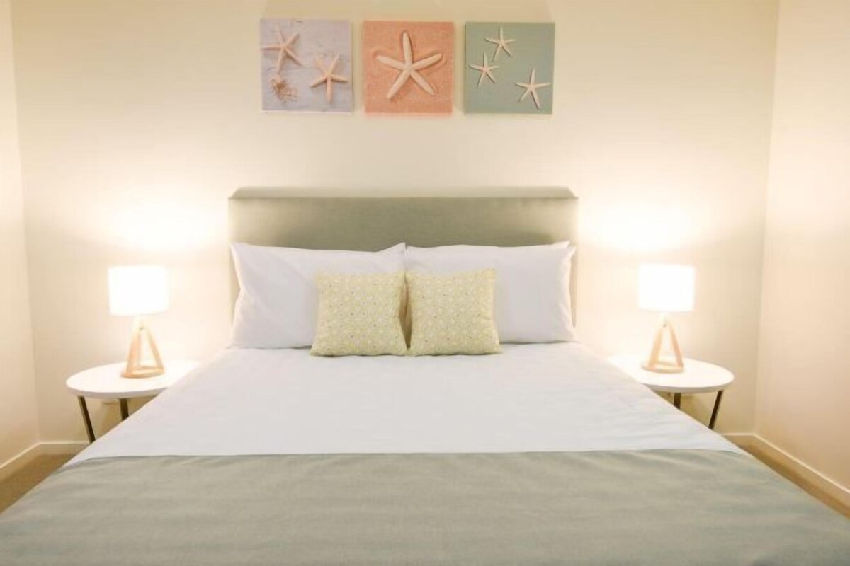 A neatly made bed with two pillows, two bedside lamps, and three starfish wall art pieces.