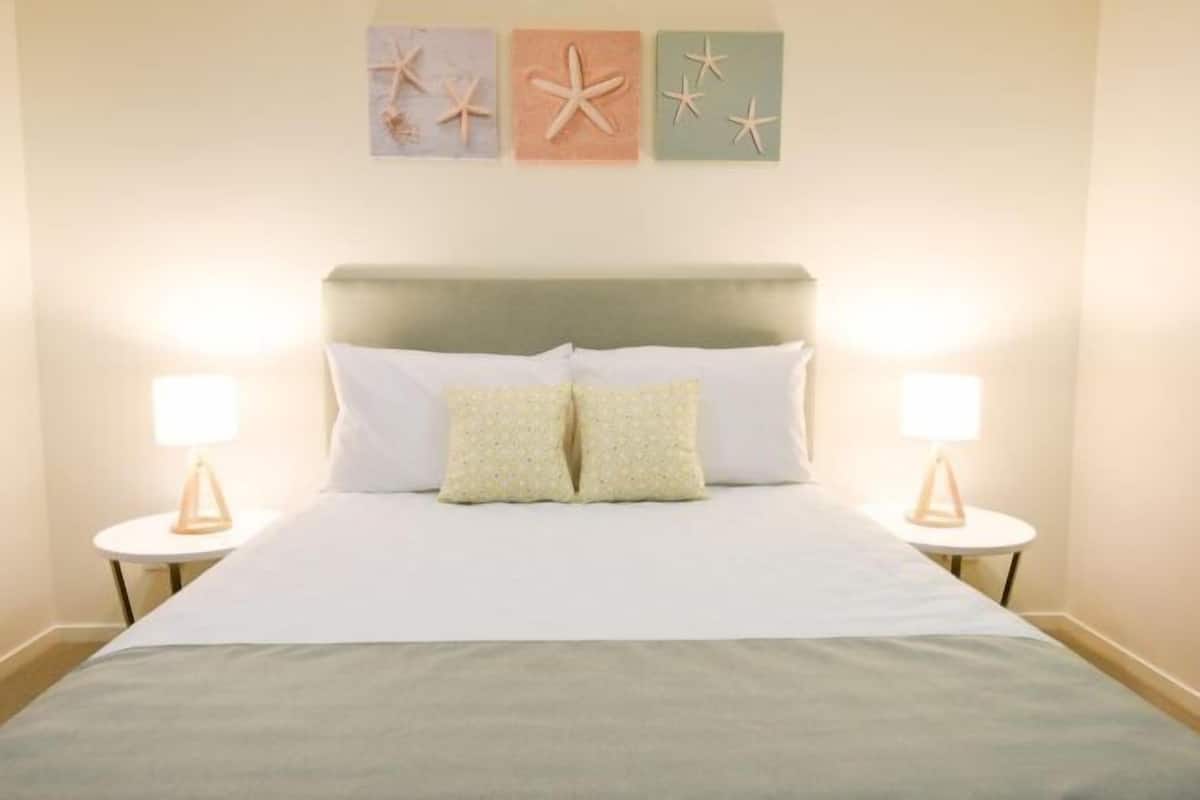 A neatly made bed with two pillows, two bedside lamps, and three starfish wall art pieces.